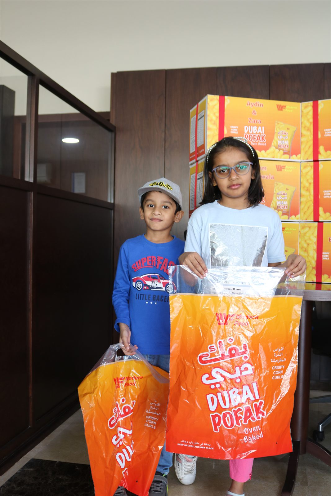 Two children indoors holding bags of Dubai Pofak