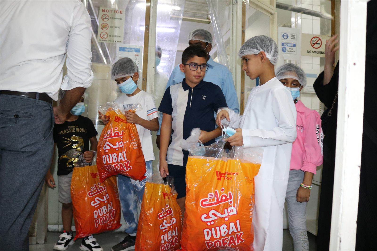 Children being handed orange Dubai Pofak bags by staff in face masks